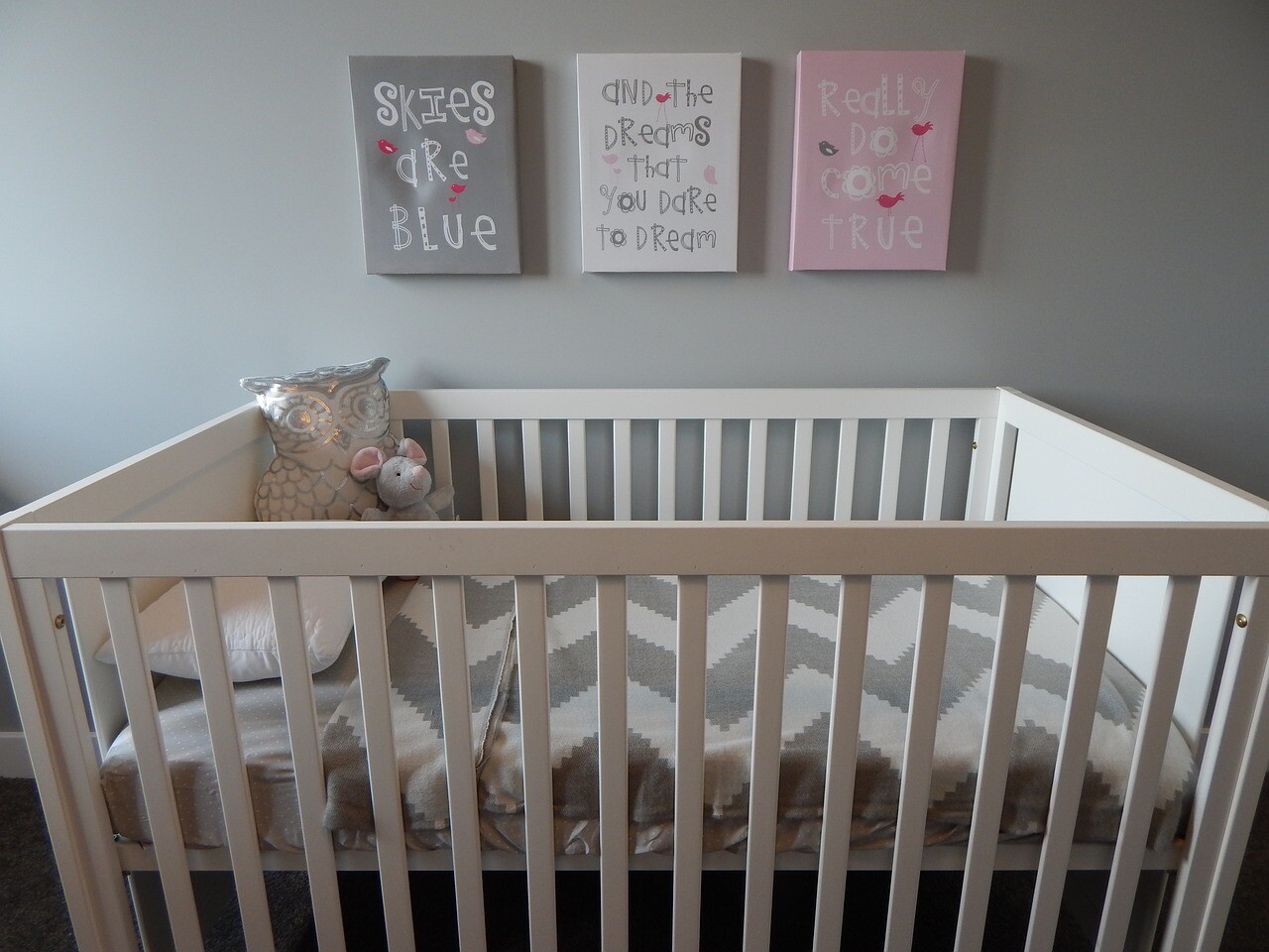 An ordinary white crib with grey and white sheets