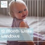 12 month old wake window example: 12 month old baby sitting up smiling on bed